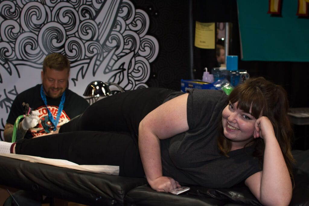 Woman smiling while getting tattooed at convention.