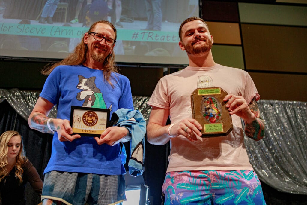 Two tattoo artists holding award plaques.