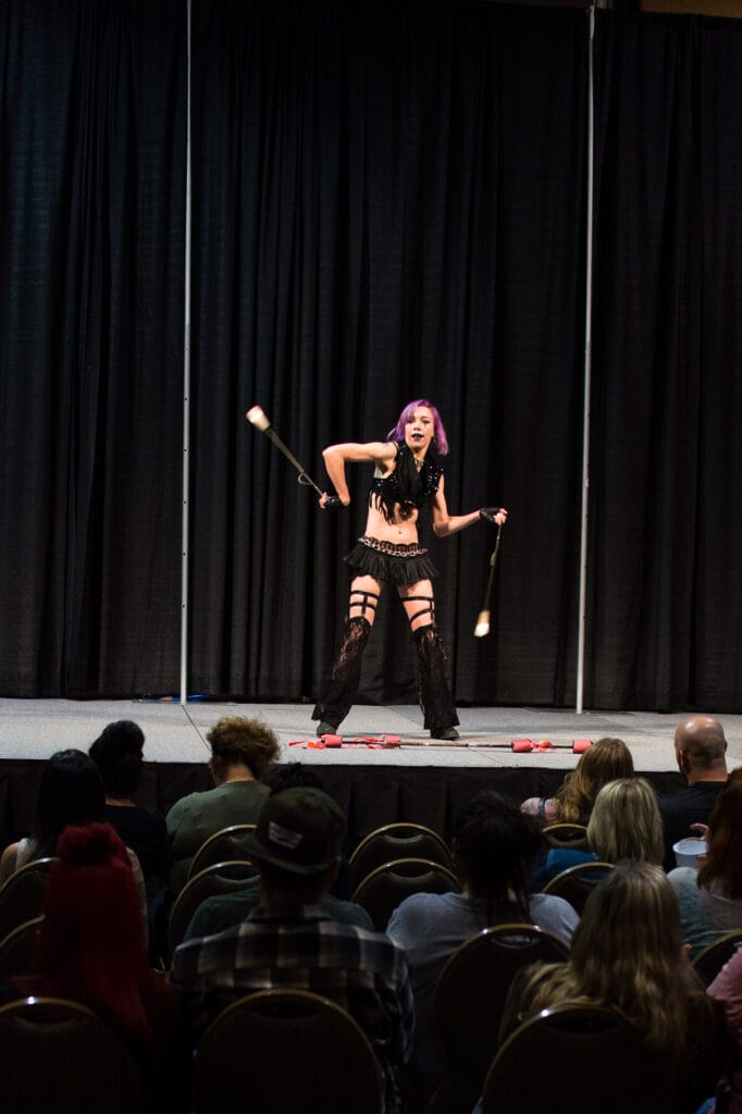 Performer with purple hair juggling on stage.
