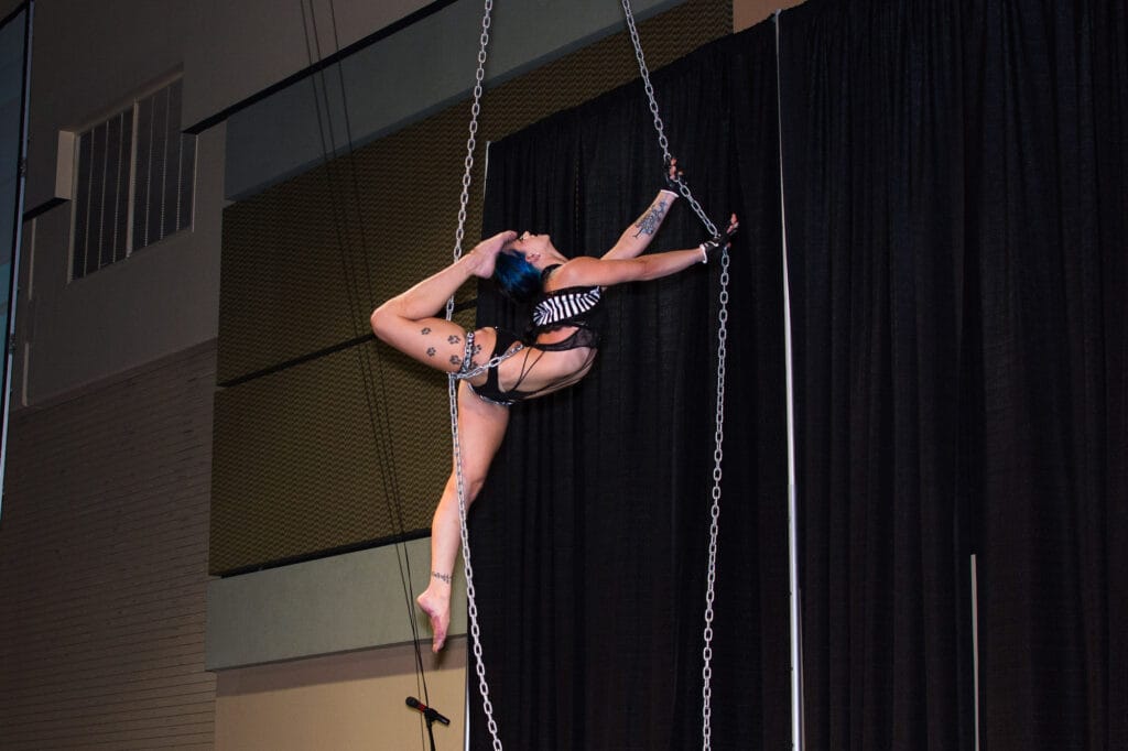 Aerial performer suspended on chains during acrobatic act.