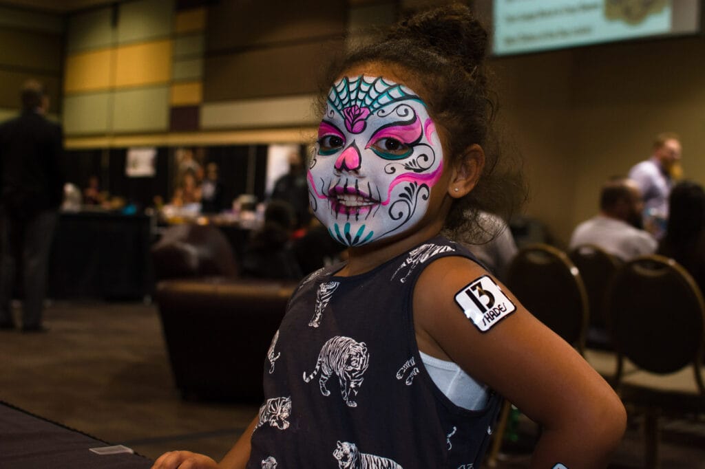 Child with colorful face paint at indoor event.