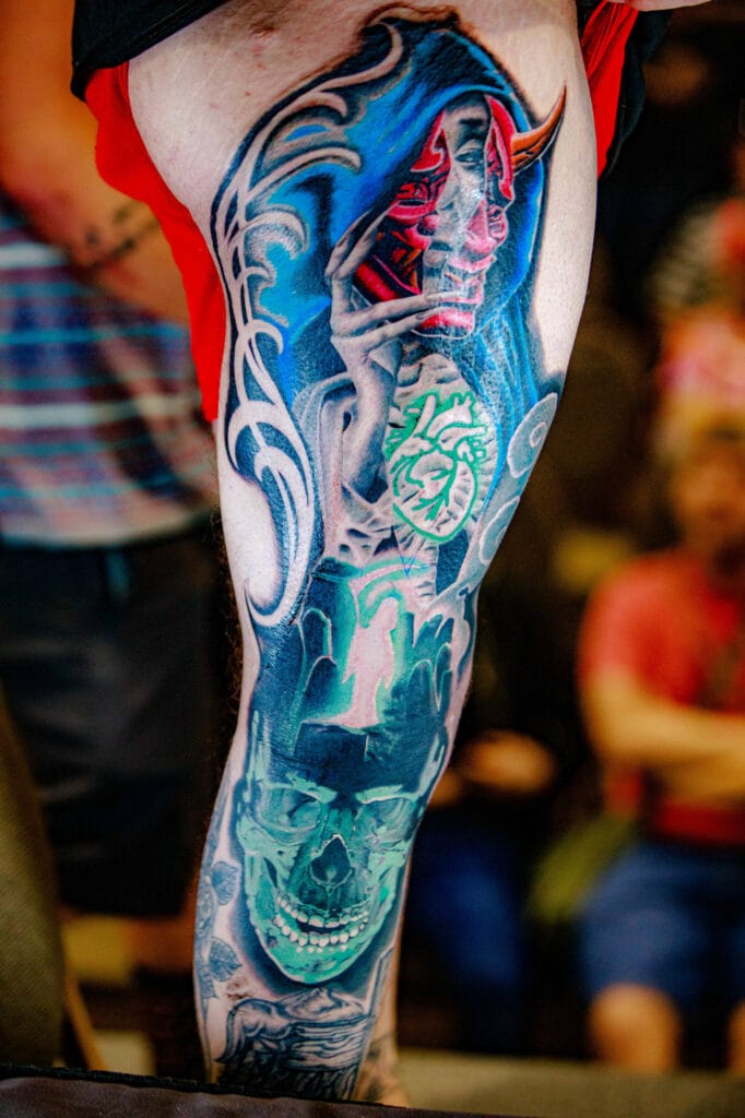 Colorful leg tattoo with skull and demon mask design.