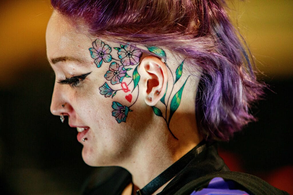 Woman with colorful floral face tattoo, purple hair.