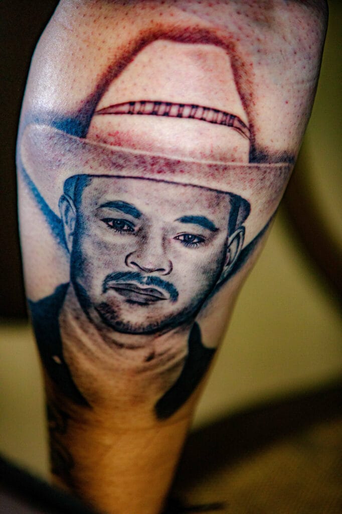 Portrait tattoo of man wearing cowboy hat.