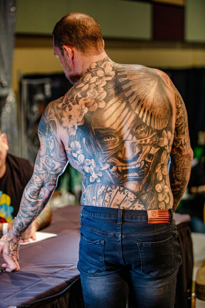 Man with intricate back tattoo at tattoo convention.