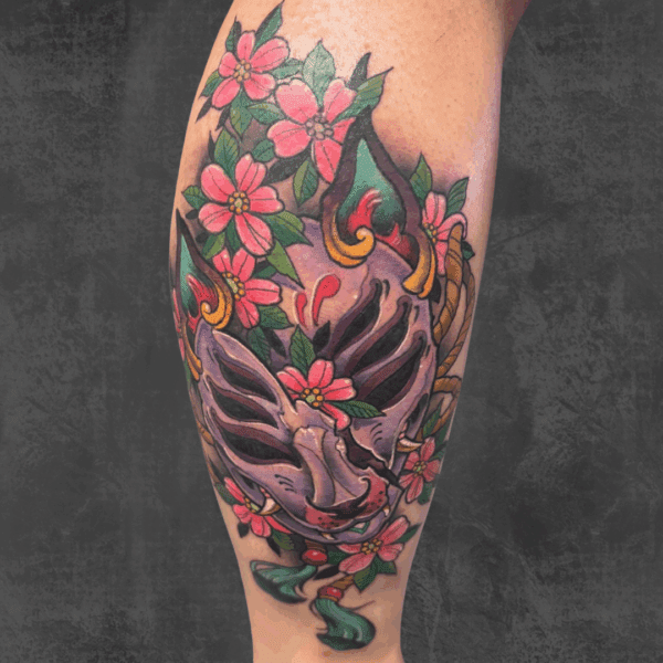 Colorful Oni mask tattoo with pink flowers.